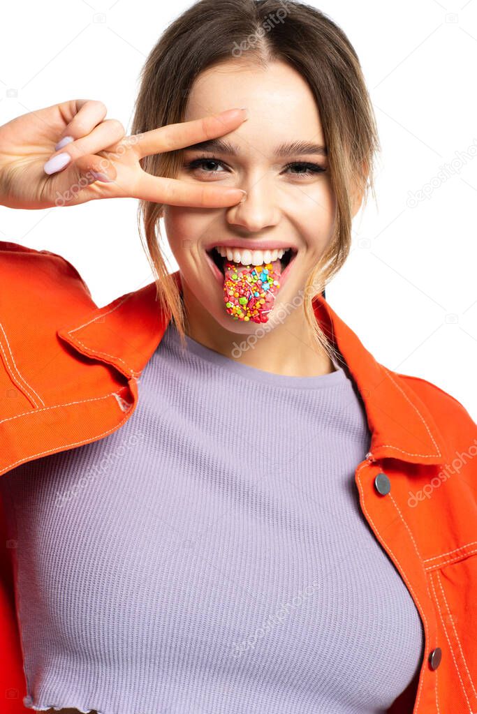 young woman sticking out tongue with tasty sprinkles and showing peace sign isolated on white 