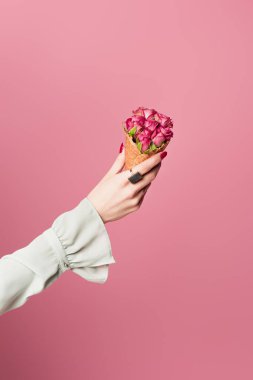 Cropped view of woman holding waffle cone with blooming flowers isolated on pink  clipart