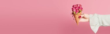 Cropped view of woman holding waffle cone with roses in hand isolated on pink, banner  clipart