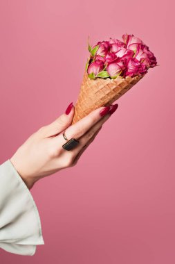 Yüzüğü parmağında, elinde lezzetli bir waffle külahı ve pembe üzerine izole edilmiş güller tutan kadın görüntüsü. 