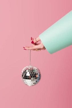 Kırmızı manikürlü ve aksesuarlı bir kadın disko topunu pembe üzerine izole bir şekilde tutuyor. 