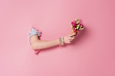 Cropped view of woman holding delicious waffle cone and rose flowers in hole of pink background  clipart