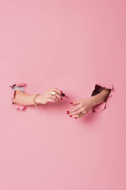 Pembe arka planda tırnak cilası sürerken kadının kısmi görüntüsü 