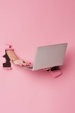 Pembe arka planda, aksesuarları olan, dizüstü bilgisayar kullanan bir kadının kısmi görüntüsü 