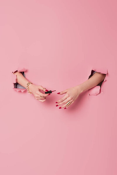 Cropped view of woman holding applicator with nail polish near pink background with holes 