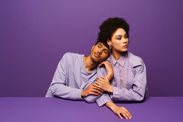 african american man leaning on young curly woman isolated on purple