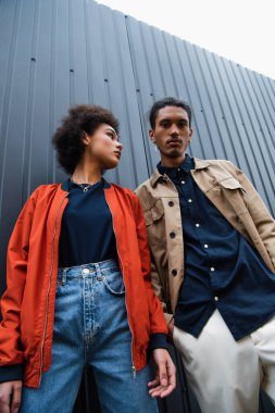 low angle view of african american couple in trendy jackets posing outside  clipart