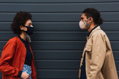 Genç Afrikalı Amerikalı kadın ve koruyucu maskeli şık bir adam dışarıda birbirlerine bakıyorlar. 