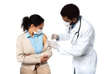 Afro-Amerikalı doktor beyaz maskeli hastaya aşı enjekte ediyor. 