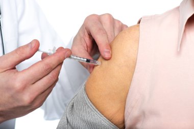 Beyazlar içinde izole edilmiş yaşlı bir hastaya aşı enjekte edilirken görüntülenmiş. 