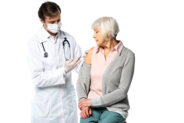 Tıbbi maske takan doktor beyazlar içinde izole edilmiş yaşlı hastaya aşı enjekte ediyor. 