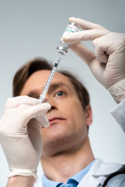Aşı ve şırınganın düşük açılı görüntüsü gri renkli bulanık doktorun ellerinde. 