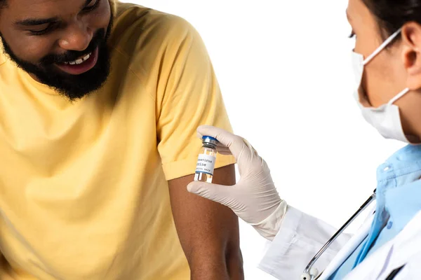 医生手中拿着的疫苗在朦胧的前景中接近面带微笑的非洲裔美国病人被隔离在白色的环境中 — 图库照片