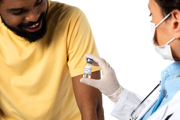 Vaccine in hand of doctor on blurred foreground near smiling african american patient isolated on white 