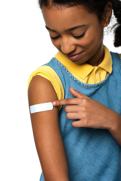 Smiling african american kid looking at adhesive patch on arm isolated on white 