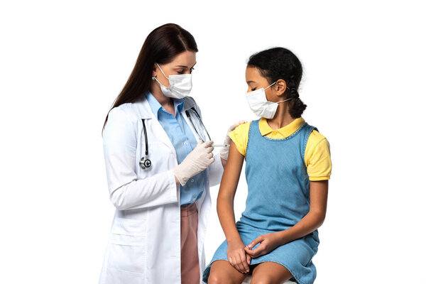 Pediatrician in medical mask doing vaccine injection to african american child isolated on white 