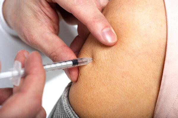 Close up view of doctor doing injection with vaccine to senior woman isolated on white 