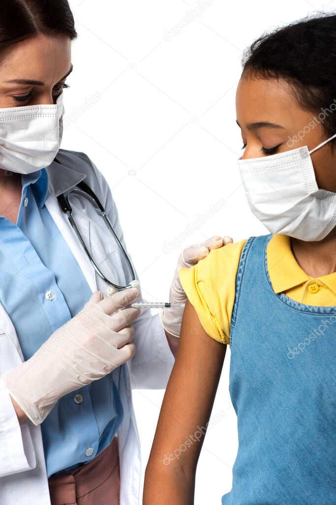 Doctor doing injection with vaccine to african american kid in medical mask isolated on white 