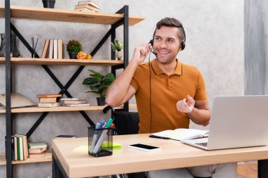 Evde çalışan kulaklıklı neşeli bir adam. Temiz bir laptop ve boş ekranlı akıllı telefon.