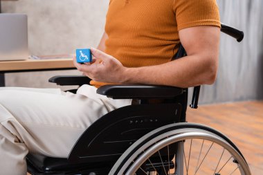Tekerlekli sandalyede elinde engelli işareti olan bir adam.