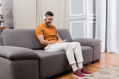 Neşeli adam kulaklıkla müzik dinlerken cep telefonuyla mesajlaşıyor.