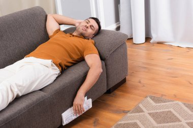 Genç adam elinde gazeteyle kanepede uyuyor.