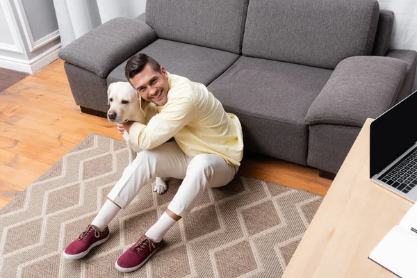 Young Man Smiling Camera While Hugging Labrador Floor Desk Laptop — Stock Photo, Image