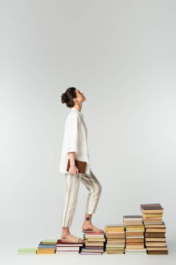 Genç, dövmeli bir kadının beyaz kitapların üzerinde dikilirken yukarı baktığı yan manzara. 