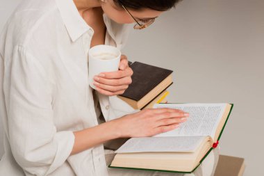 Gözlüklü genç esmer kadın kitap okuyor ve elinde bir fincan kahve tutuyordu. 