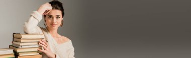 Küpeli genç bir kadın Gri, afiş üzerine kitap yığınına yaslanıyor