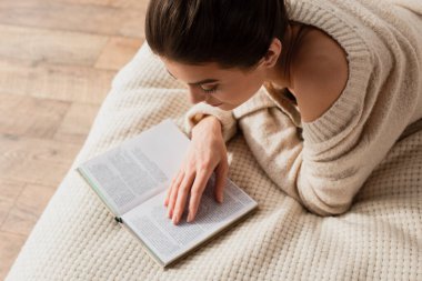 Yatakta dinlenirken kitap okuyan genç bir kadının yüksek açılı görüntüsü