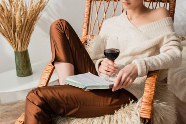 Sallanan sandalyede kitap ve şarapla oturan genç bir kadın manzarası.