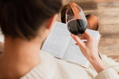 Bulanık genç bir kadın kitap okuyor ve elinde bir kadeh kırmızı şarap tutuyor.