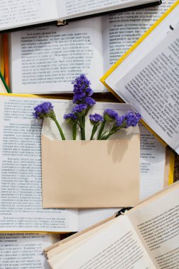Mor çiçeklerin üst görünümü kitap yığınının üzerindeki zarfın içinde 
