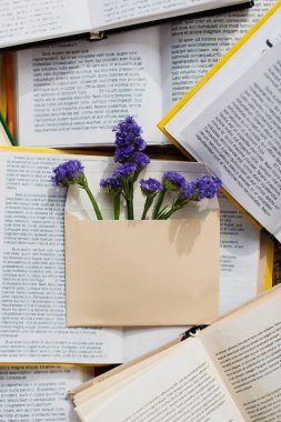 top view of purple blooming flowers in envelope on pile of books  clipart