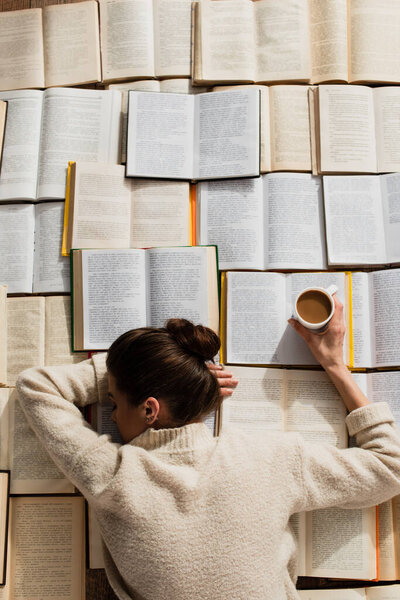 top view of pretty woman sleeping near open books with cup of coffee