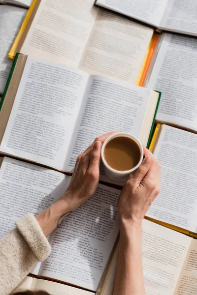 Açık Kitapların Yanında Elinde Kahve Fincanı Olan Bir Kadın — Stok fotoğraf
