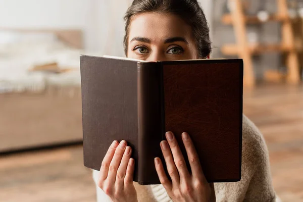 woman obscuring face while holding book and looking at camera