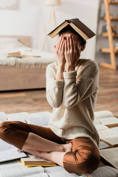 本の山の上に座って顔を隠している若い女性 — ストック写真