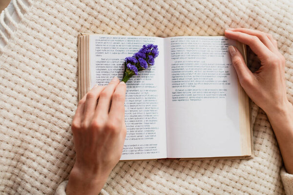 top view of young woman reading book with purple flower 