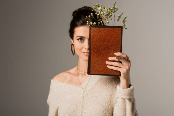 young woman holding book in hardcover with flower isolated on grey 