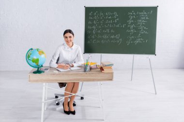 Gülümseyen öğretmen dünyanın yakınındaki deftere ve kitaplara yazı yazıyor. 