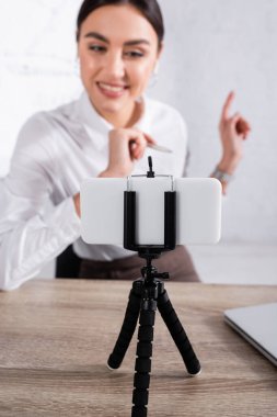 Selfie çubuğundaki akıllı telefon gülümseyen iş kadınının yanında bulanık bir arkaplanda video görüşmesi yapıyor. 