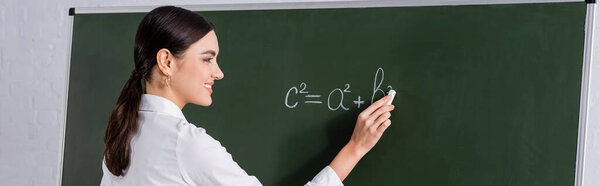 Smiling teacher writing equation on chalkboard, banner 