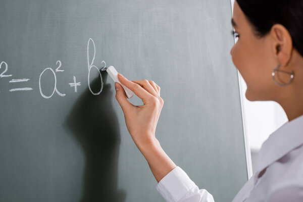 Blurred teacher writing mathematic formula on chalkboard 