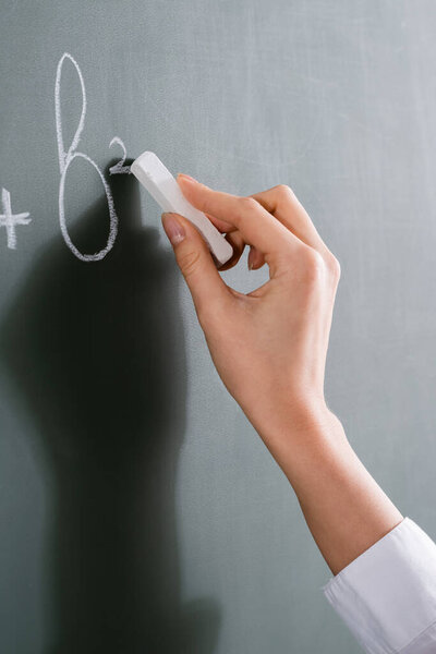 Обрезанный взгляд учителя с мелом написания математической формулы на доске 