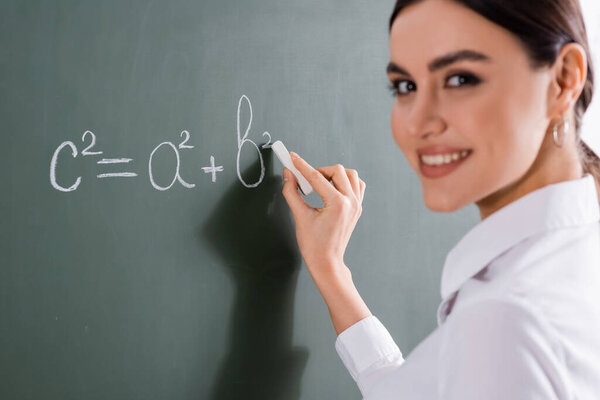 Blurred teacher smiling at camera while writing mathematic formula 