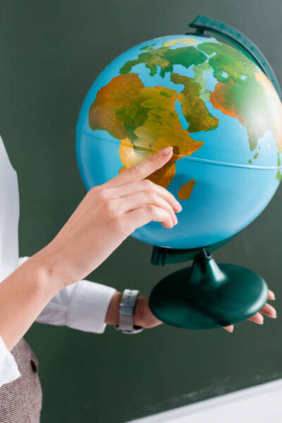 Cropped view of teacher pointing with finger at globe 