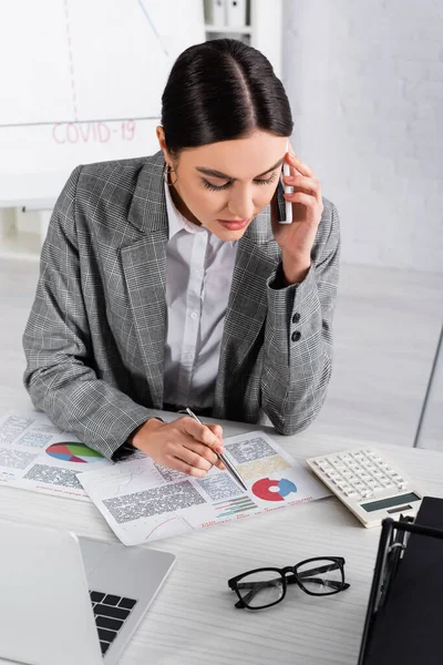 オフィスで文書上のチャートを見て スマートフォンで話すビジネスマンの女性 — ストック写真