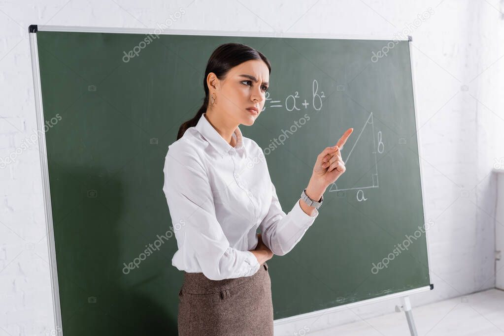 Angry teacher pointing with finger near chalkboard with equation